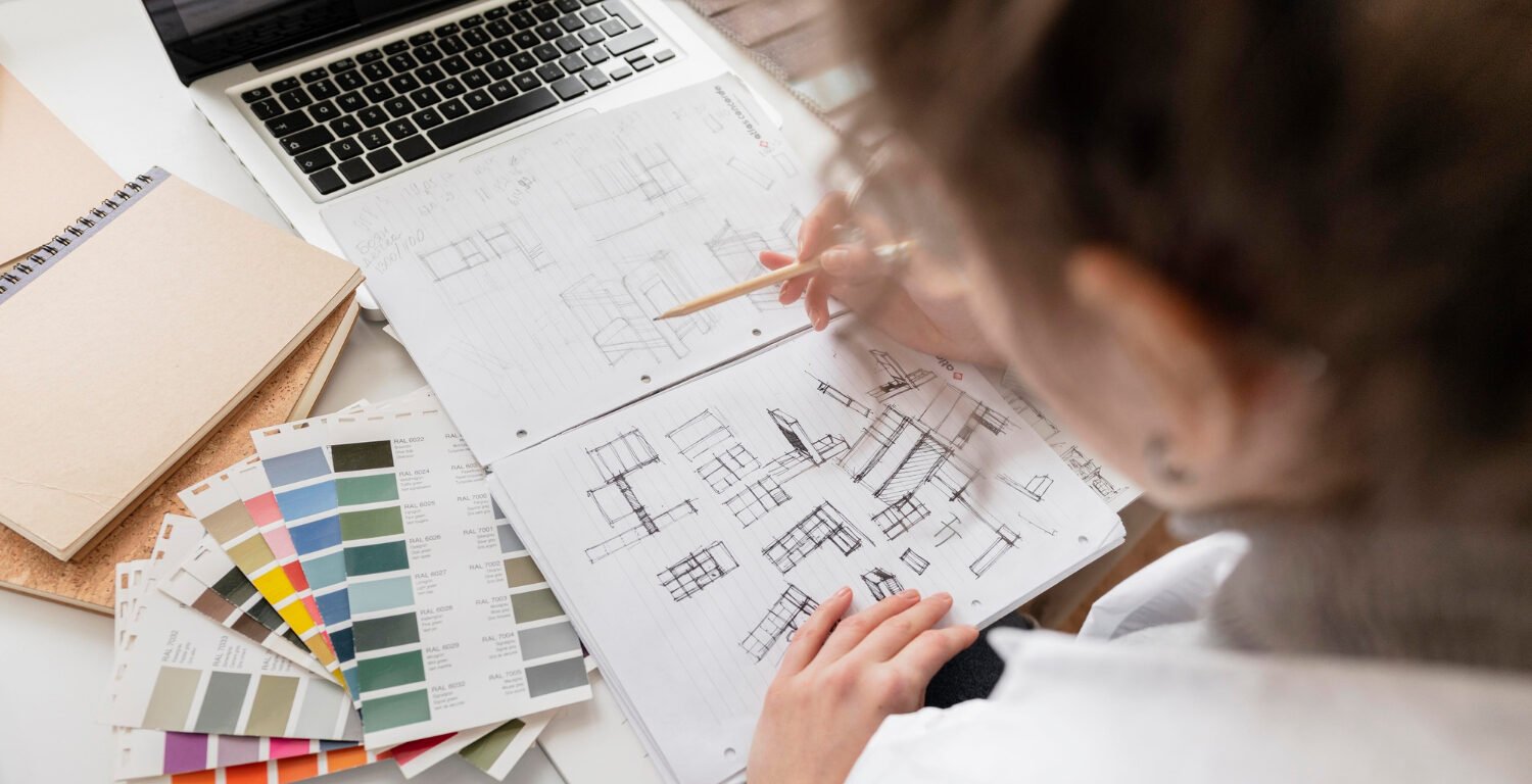 Overhead view of a woman drawing up plans with paint color samples resting next to them.