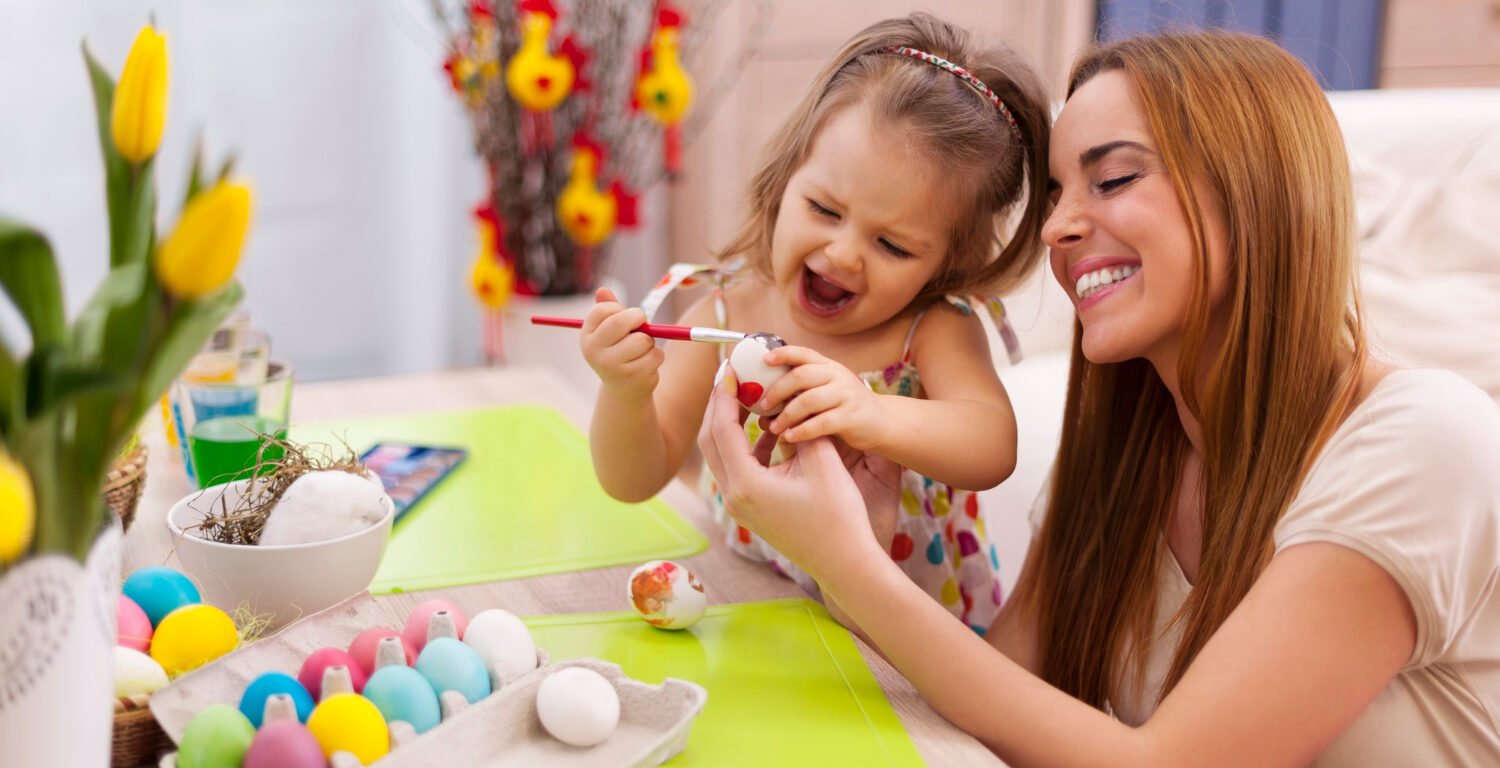 A woman and a little girl decorating eggs with paint colors. 