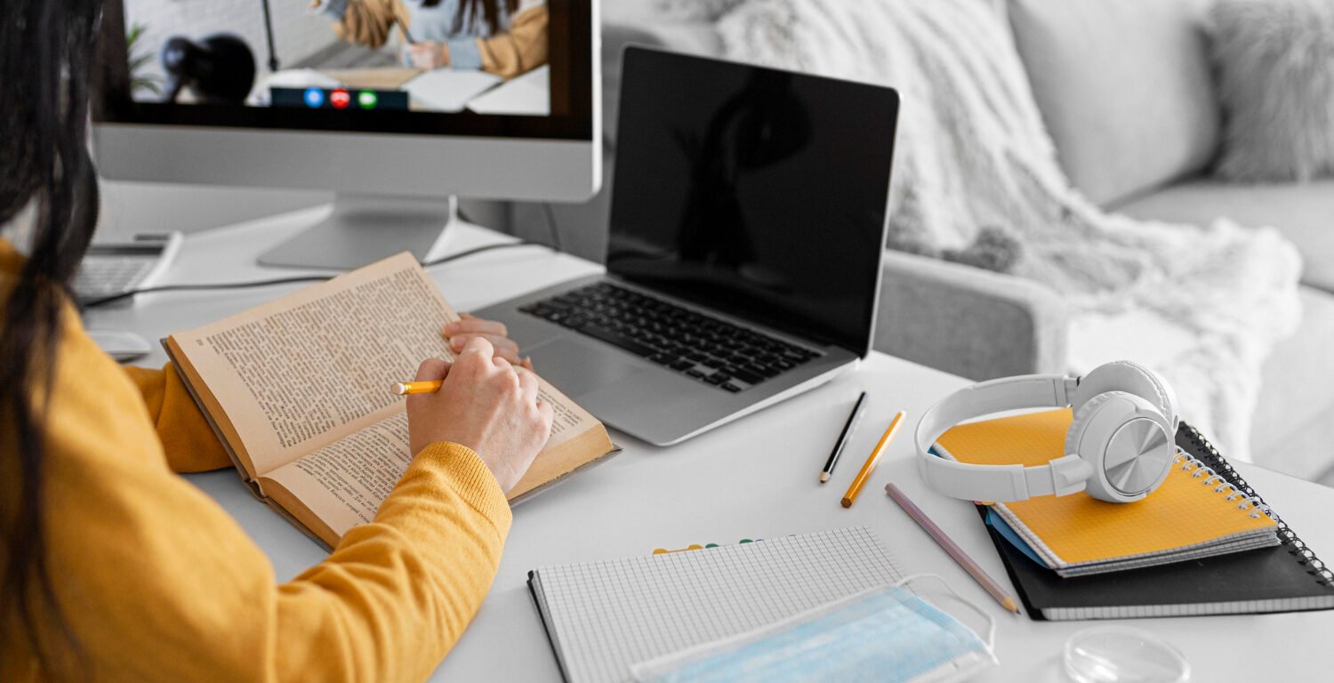 girl holding a book and taking notes while watching an online course
