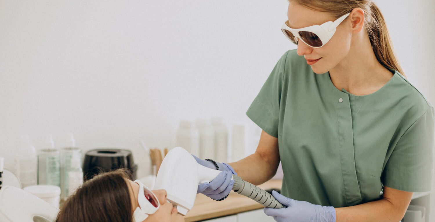 Esthetician performing laser treatment on female patient. 