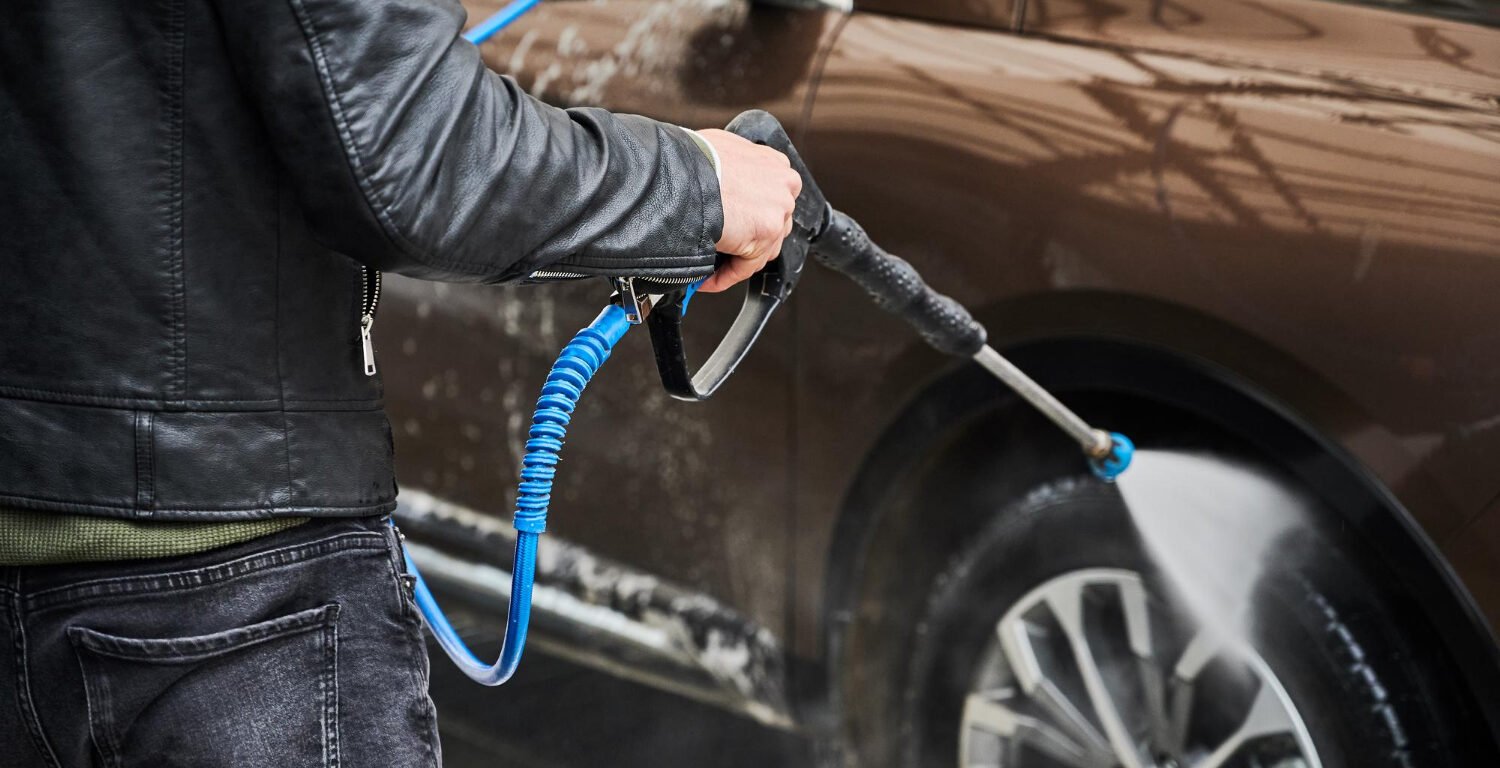 A man pressure washing the tires of a car.